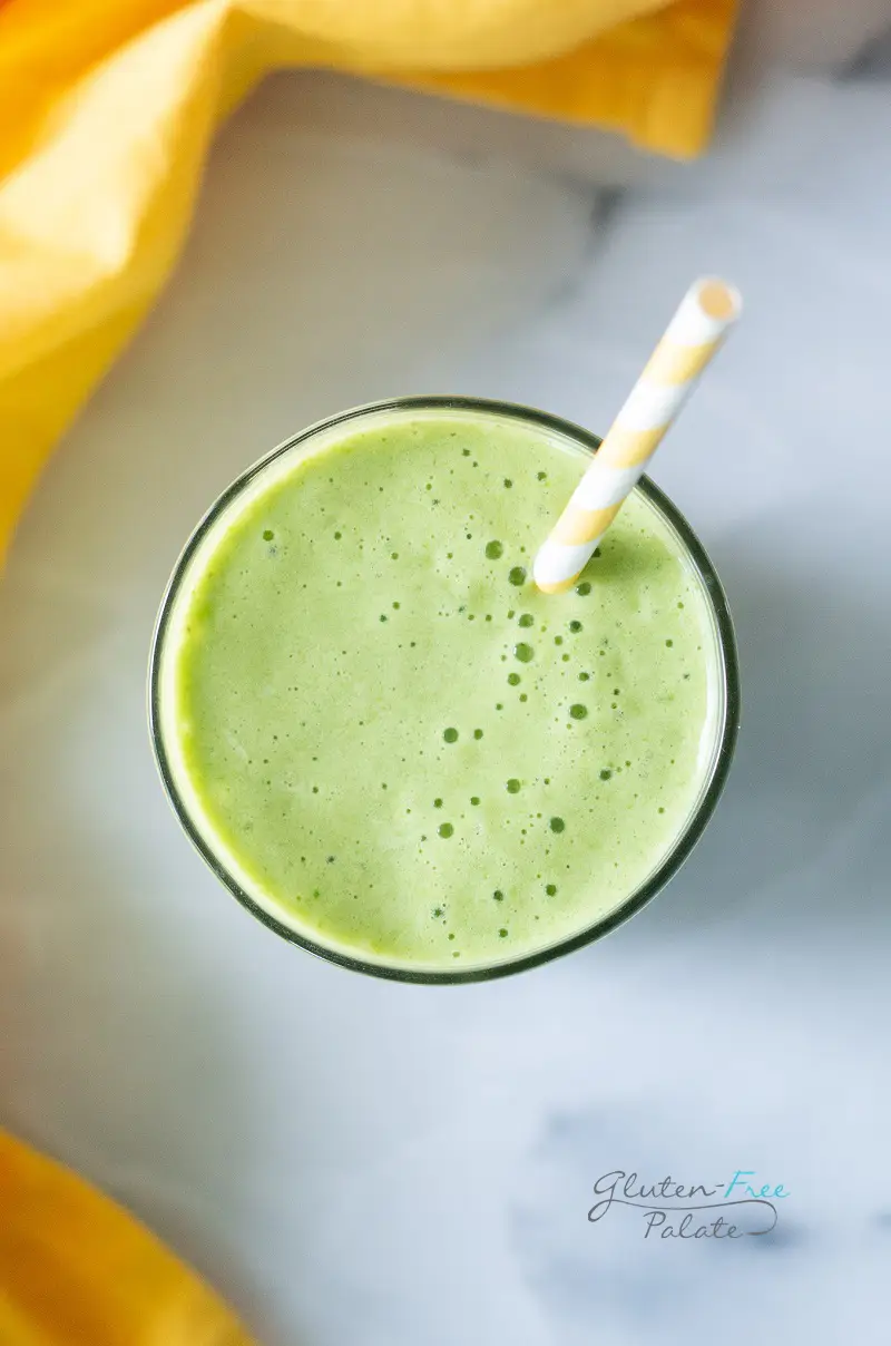 top down view of a pineapple spinach smoothie in a glass with a straw