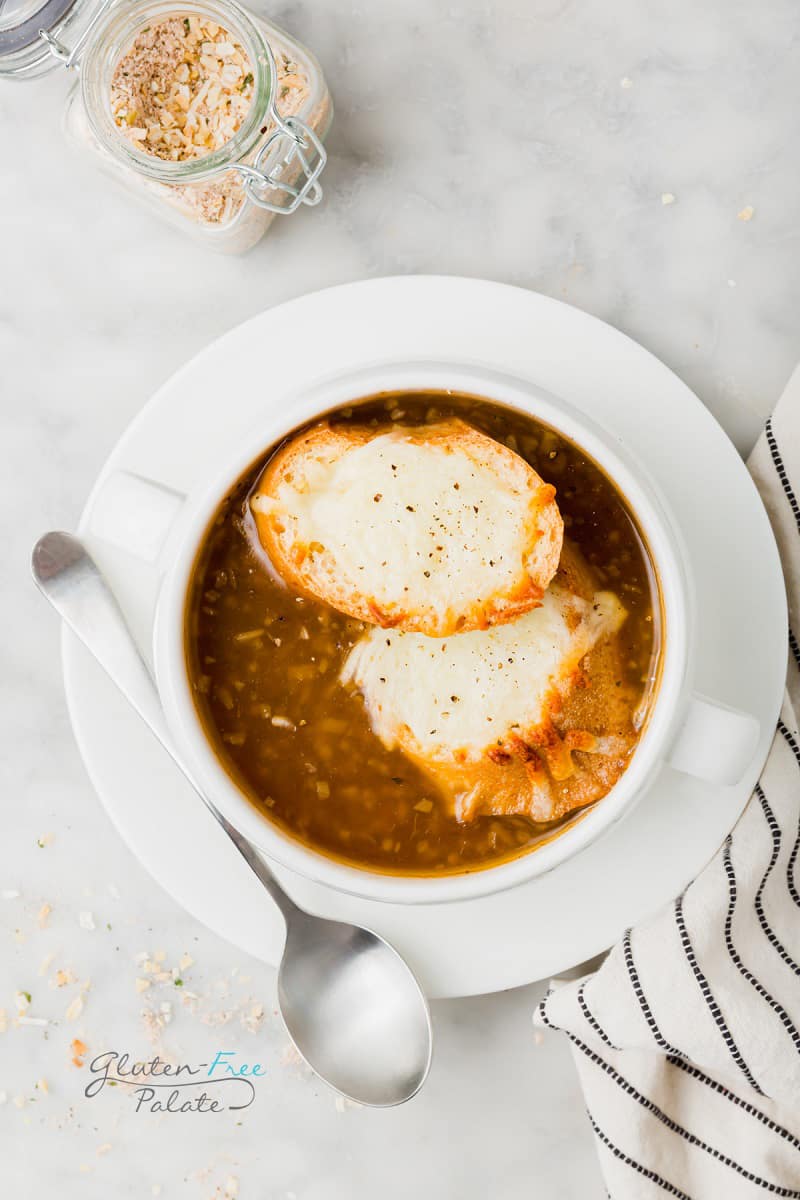 top down view of a bowl of french onion soup topped with cheesy toast, next to a jar of onion soup mix.