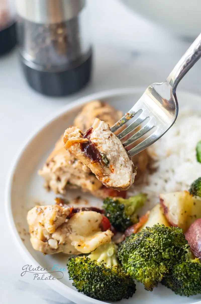 a dinner plate with rice, broccoli, potatoes and stuffed chicken breast. A bite of chicken is being lifted by a silver fork.