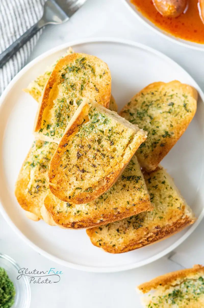 Top down view of a white plate stacked with gluten-free garlic bread halves