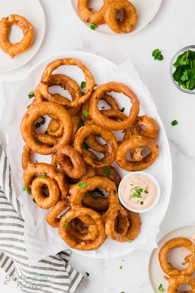 an oval platter of battered onion rings with a side of creamy dip.