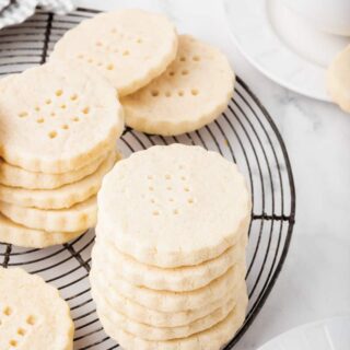 stacks of scalloped round gluten-free shortbread cookies on a round, black cooling rack.