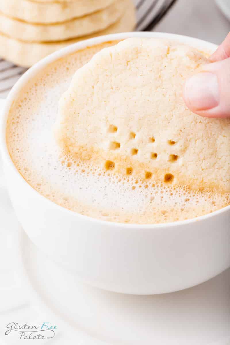 a frothy cup of coffee with a gluten-free shortbread cookie being dipped into it. 