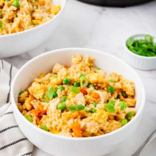 a white bowl of chicken fried rice on a marble counter next to a fork and an instant pot