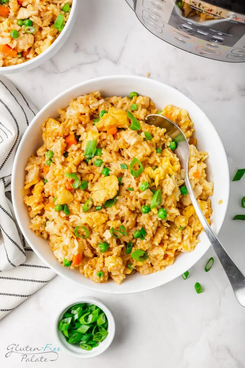 a large serving bowl filled with chicken fried rice with a spoon it it, next to an instant pot.