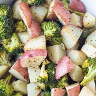 closeup view of roasted potatoes and broccoli florets in a white bowl.