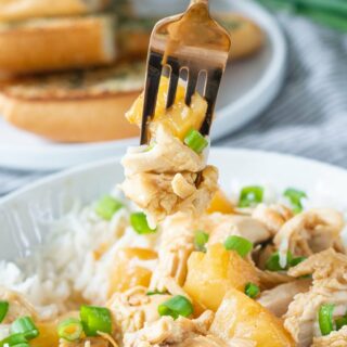Shredded Hawaiian chicken with pineapple and green onions mixed with rice, being eaten with a fork.