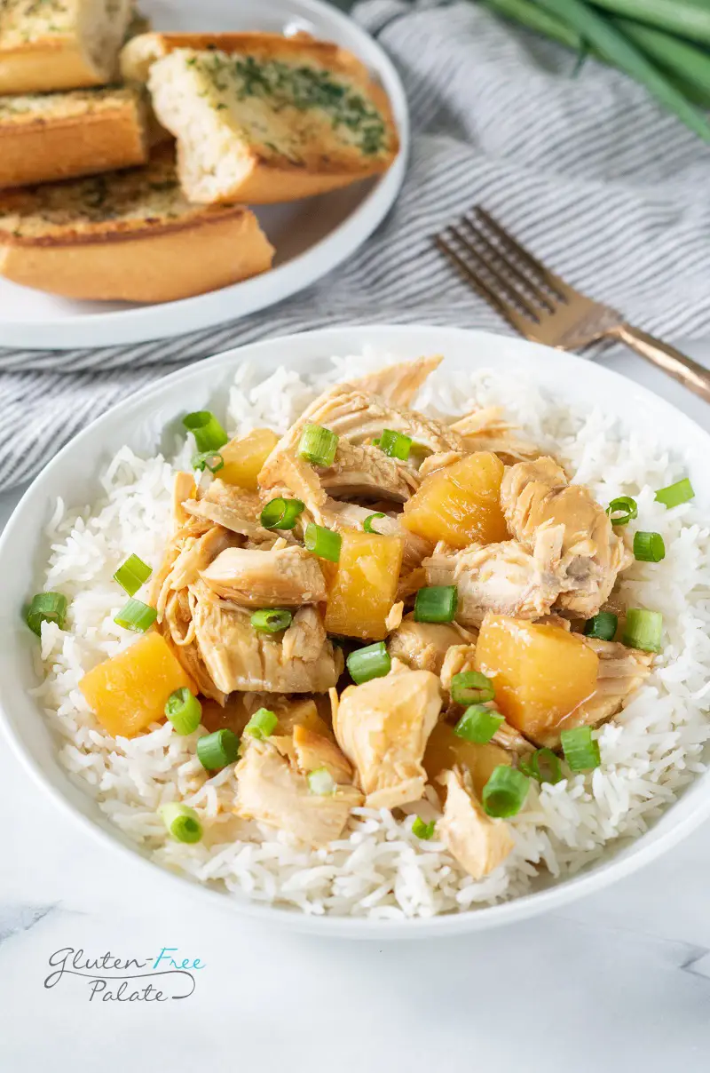 crockpot cooked chicken with pineapple on a bowl of rice, topped with scallions