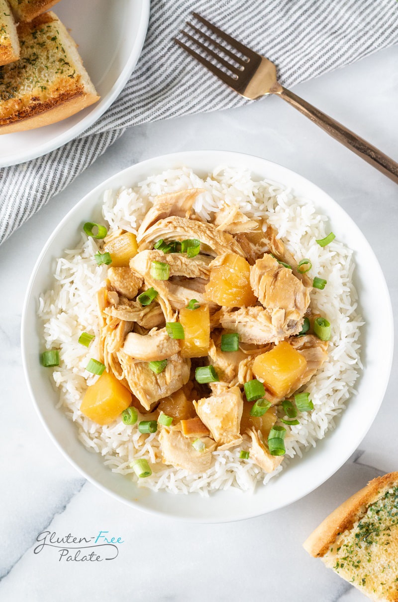 crockpot cooked chicken with pineapple on a bowl of rice, topped with scallions