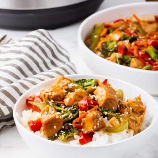 A white bowl of rice topped with chicken stir fry. Behind that is a serving bowl of the stir fry and an Instant Pot.