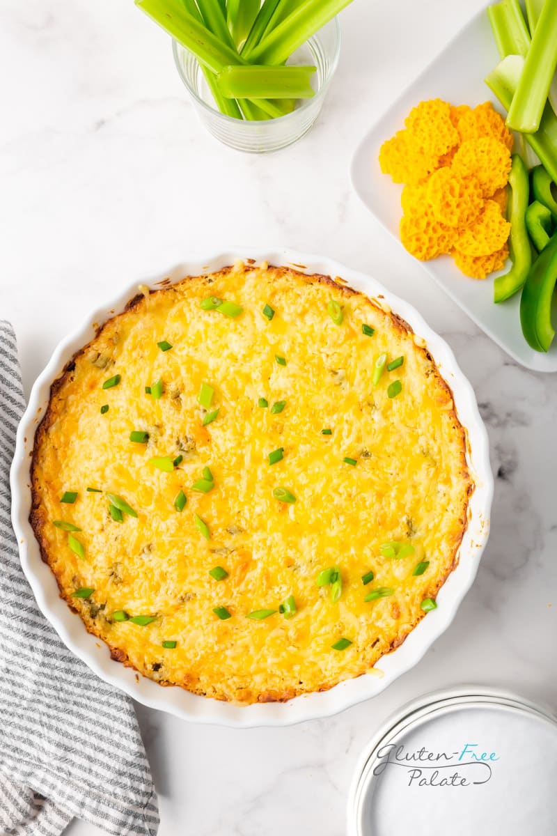 a large round dish filled with baked cheese dip and topped with green onions. Served next to a plate of cheese crisps, celery sticks and sliced green peppers