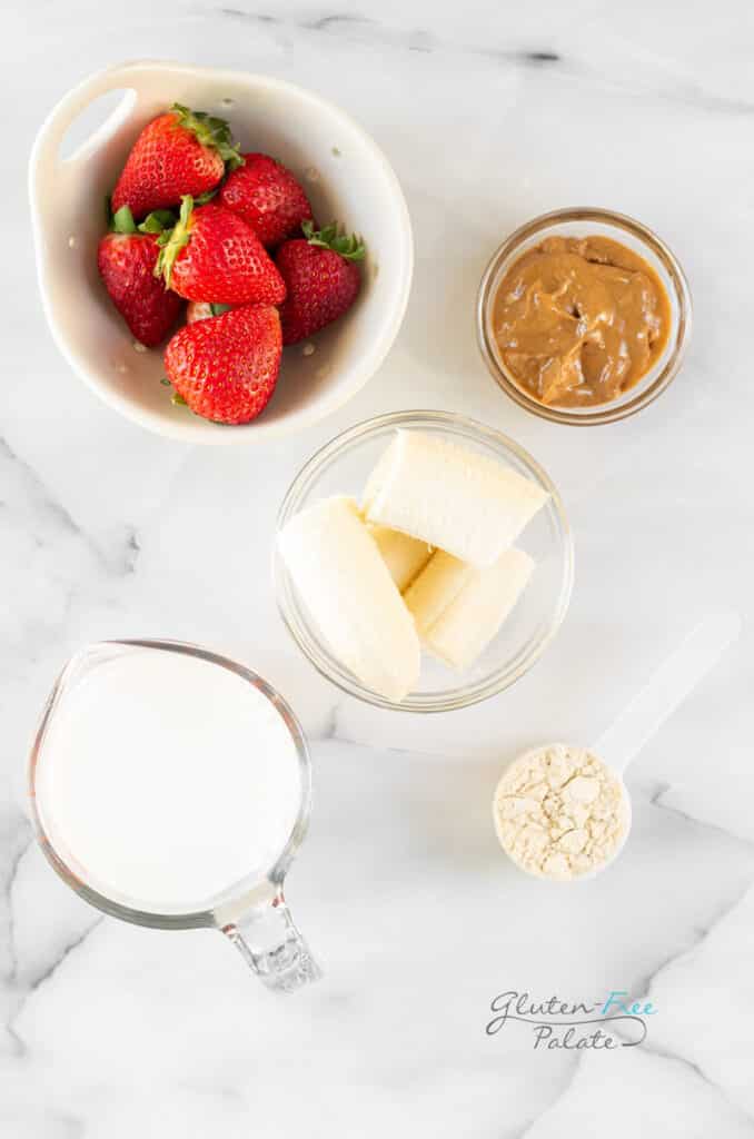 Ingredients for strawberry banana peanut butter smoothie, all in separate bowls on a marble counter.