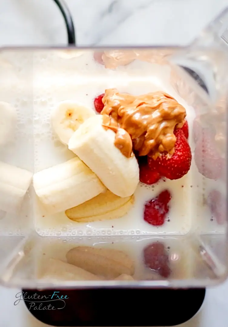 Top down view of a blender filled with milk, bananas, peanut butter, and strawberries.
