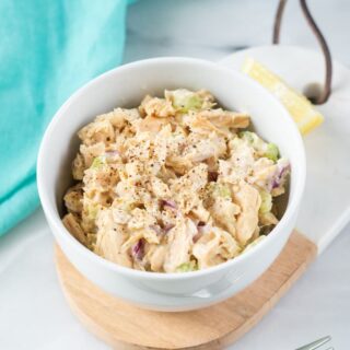 small white bowl of tuna slad on top of a wooded, oval cutting board. A fork is on the counter in front of the bowl.
