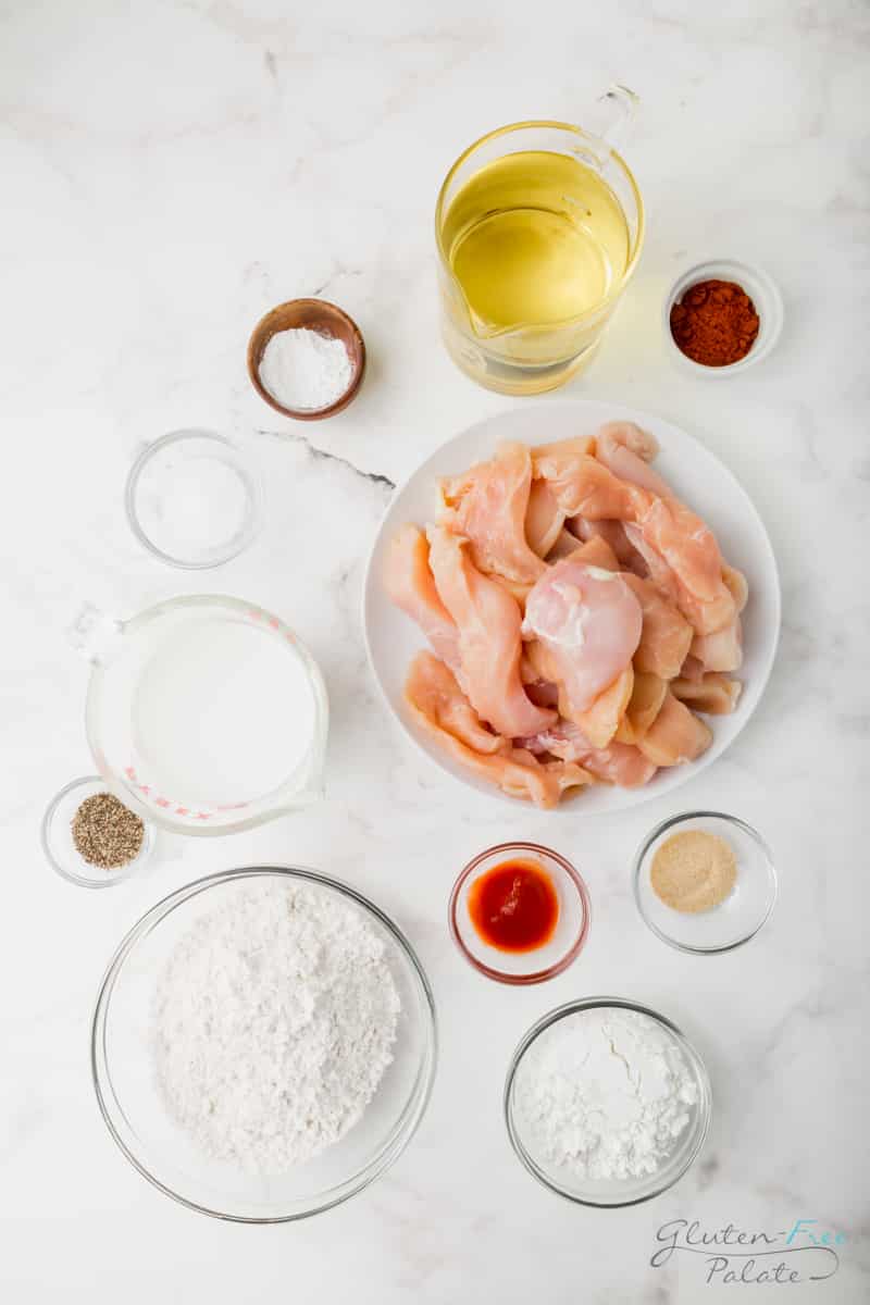 Ingredients needed to make gluten free chicken tenders, each in separate bowls on a marble countertop