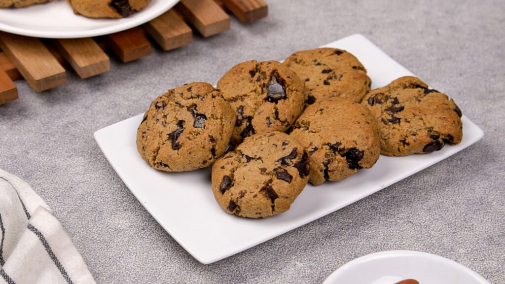 Freshly baked paleo chocolate chip cookies placed on a white plate, showing golden brown tops with melted chocolate chunks.