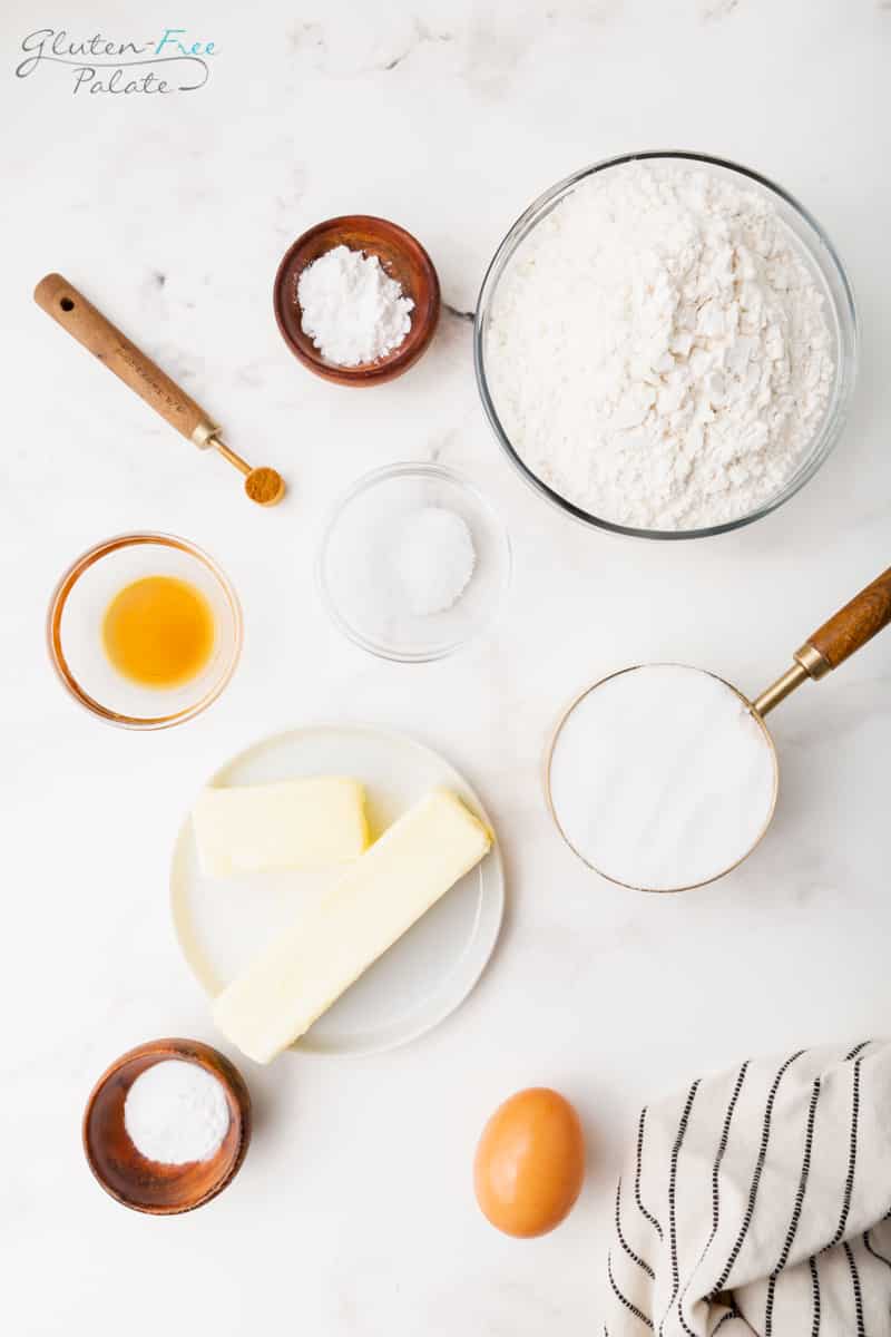 Top down view of the ingredients needed to make gluten free snickerdoodles, including a bowl of flour, one brown egg, a plate with butter, and other flavorings.