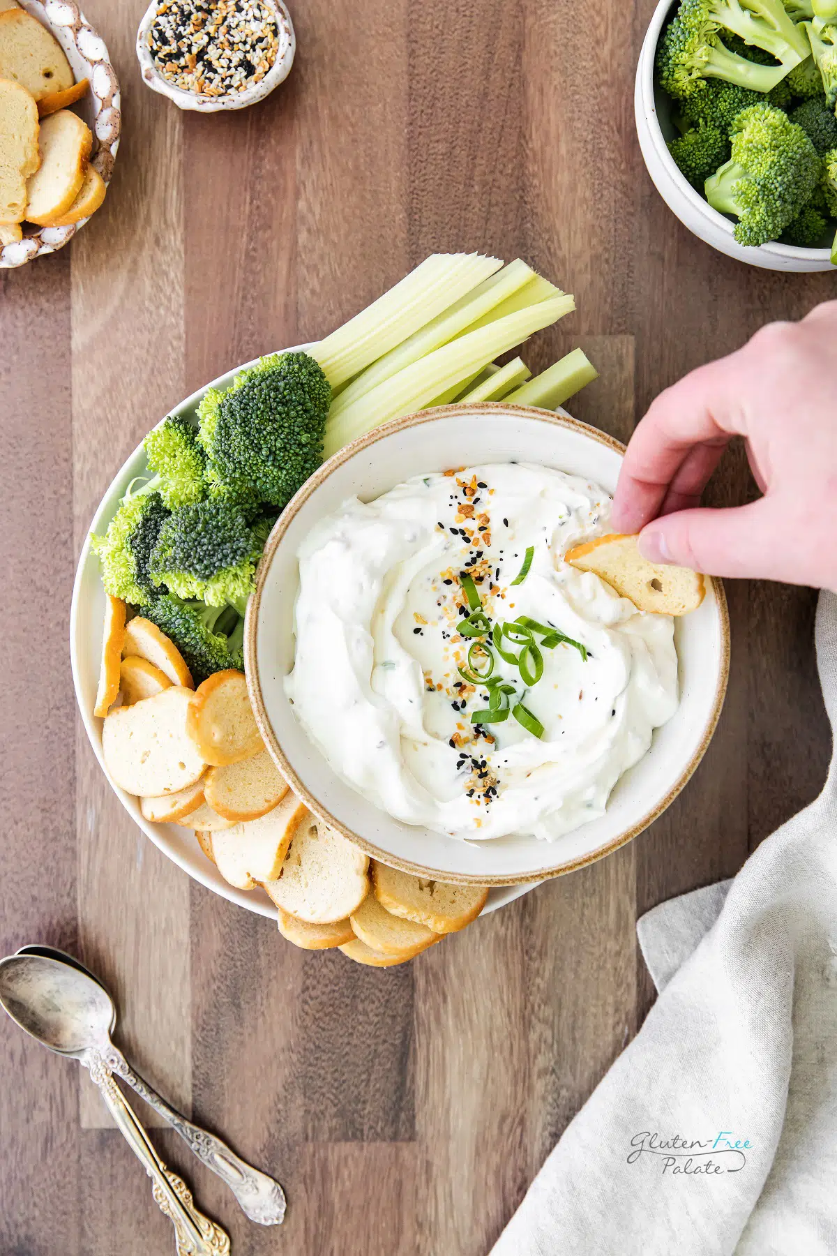 a hand dipping a bagel chip into a bowl of everything bagel dip.