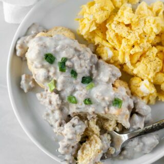 view from above of a white plate with scrampled eggs on the right and biscuits topped with sausage gravy on the left.