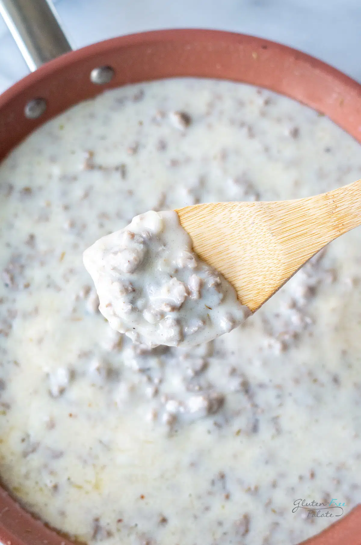 a copper skillet of creamy sausage gravy. A wooden spoon is holding some up to show texture.