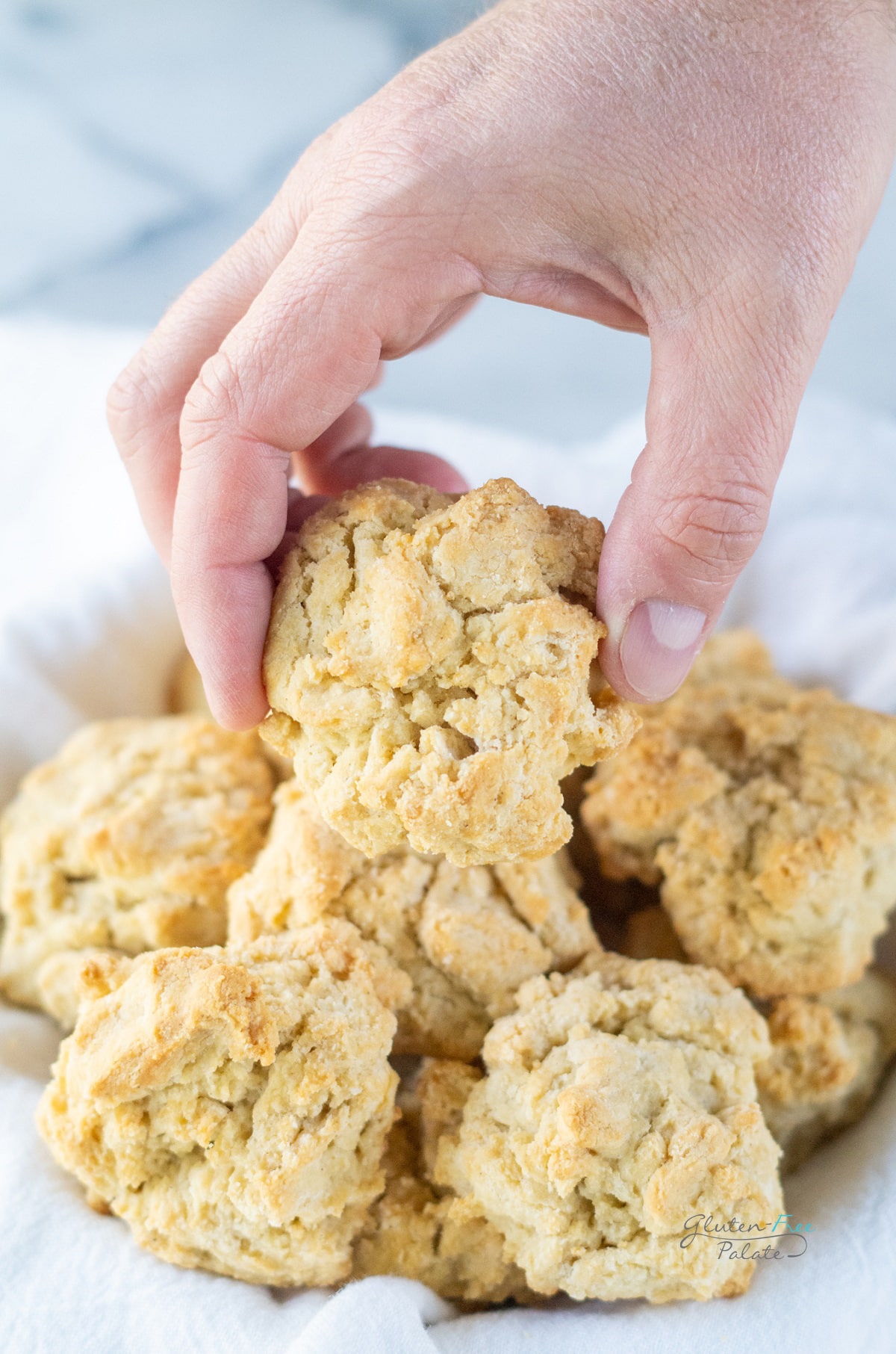 a hand is picking up a biscuit from a towel lined basket of biscuits
