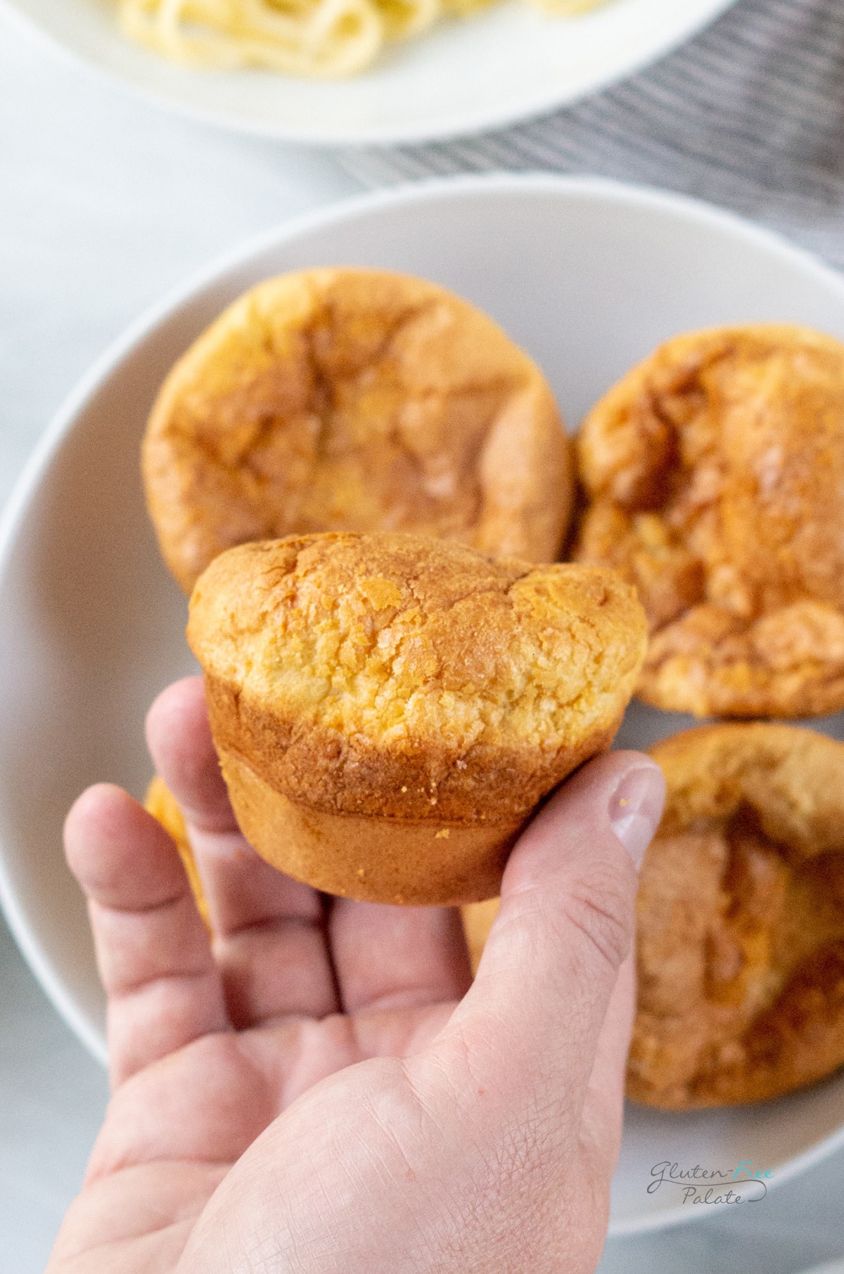 a hand holding a browned gluten free popover above a plate of them