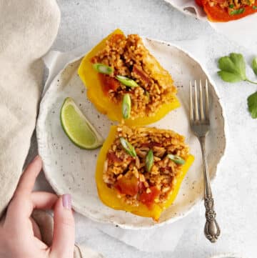 a handmade plate with two yellow stuffed peppers and a lime wedge, viewed from above