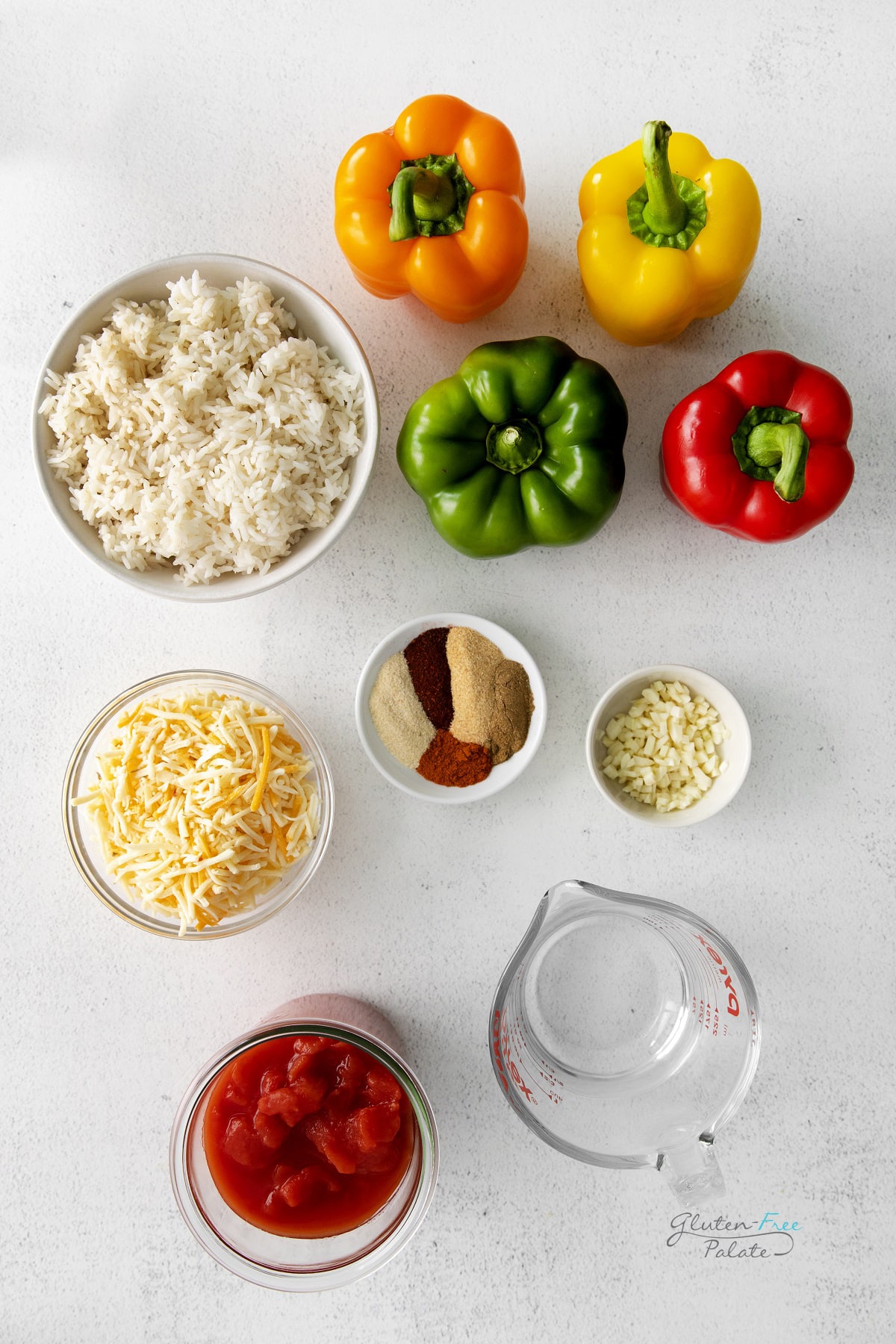 The ingredients for rice and cheese stuffed peppers on a concrete countertop, including multicolored bell peppers, seasonings, and tomatoes