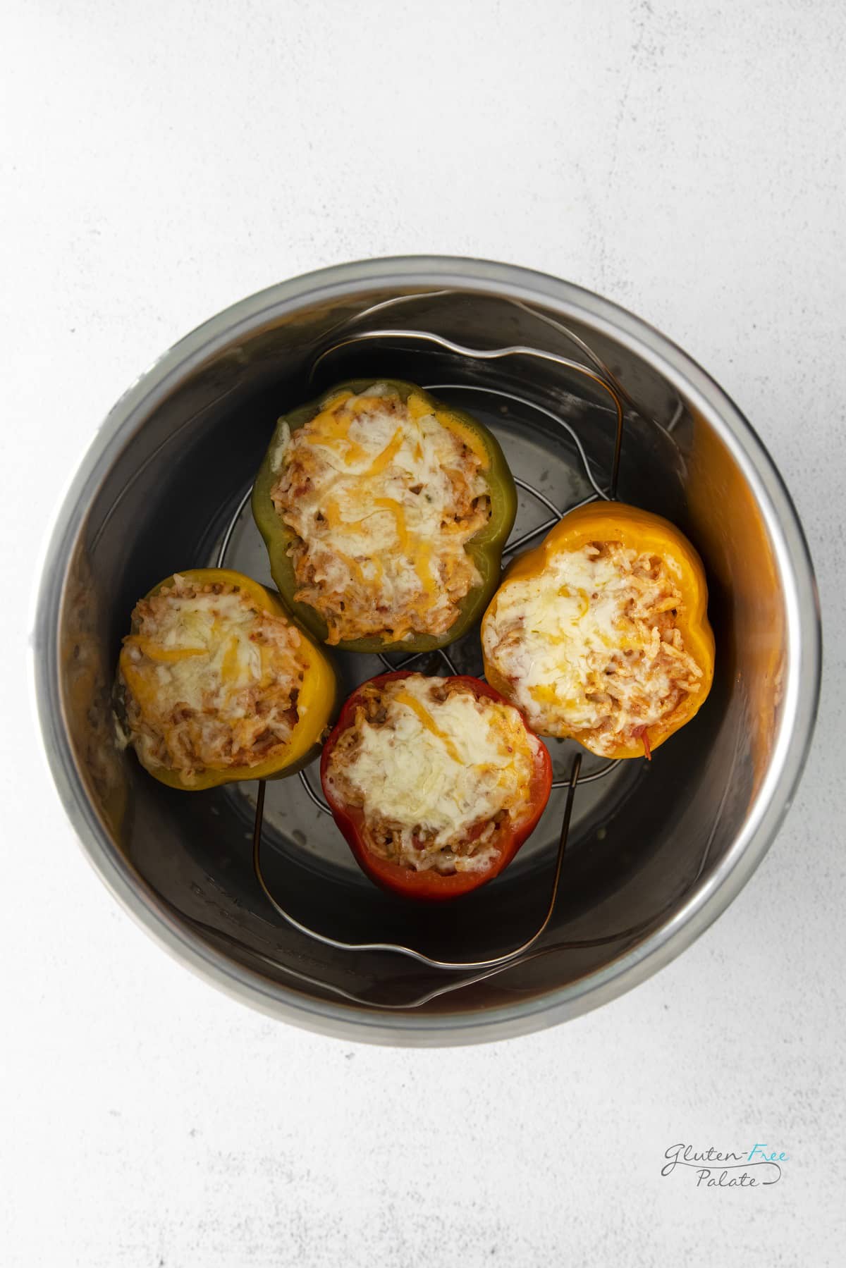 Four stuffed peppers topped with cheese inside of an instant pot, viewed from above.