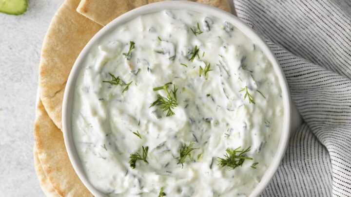 A white bowl of tzatziki dip, viewed from above, served with toasted pita and crudite