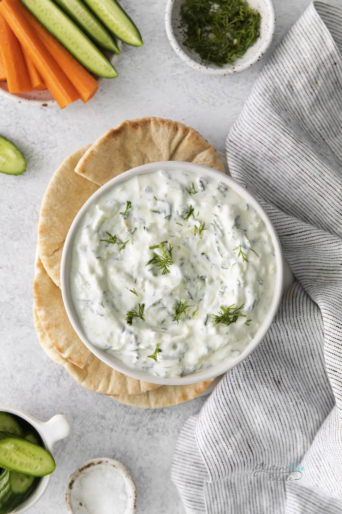 A white bowl of tzatziki dip, viewed from above, served with toasted pita and crudite