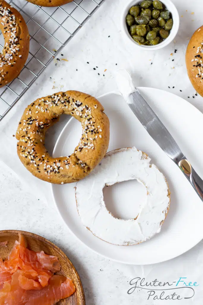 a gluten-free bagel with everything seasoning and a cream cheese spread. A knife is on the side of the plate.