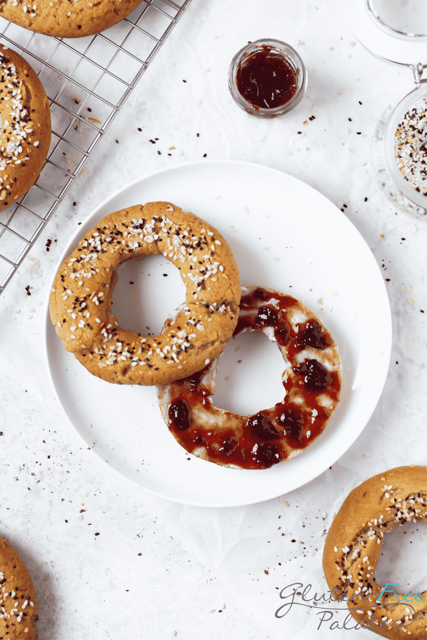 looking down at a round white plate with an everything bagel on it, sliced, filled with berry jam.