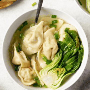 a white bowl of gluten-free wonton soup with baby bok choi