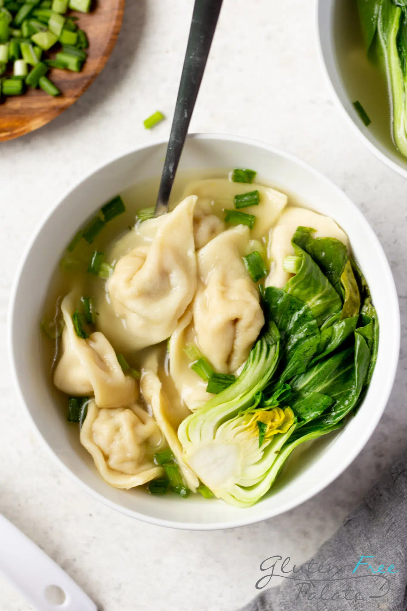 a white bowl of gluten-free wonton soup with baby Bok choi. Gluten-free wont wrappers are in the soup.