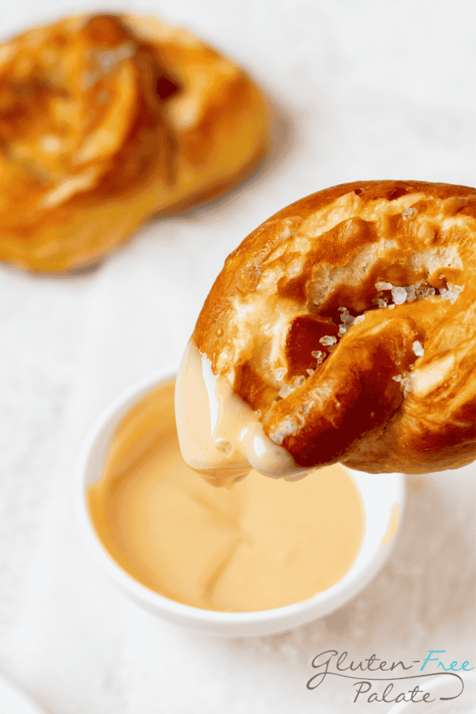 A large gluten free pretzel dipping into a small bowl of honey mustard sauce.