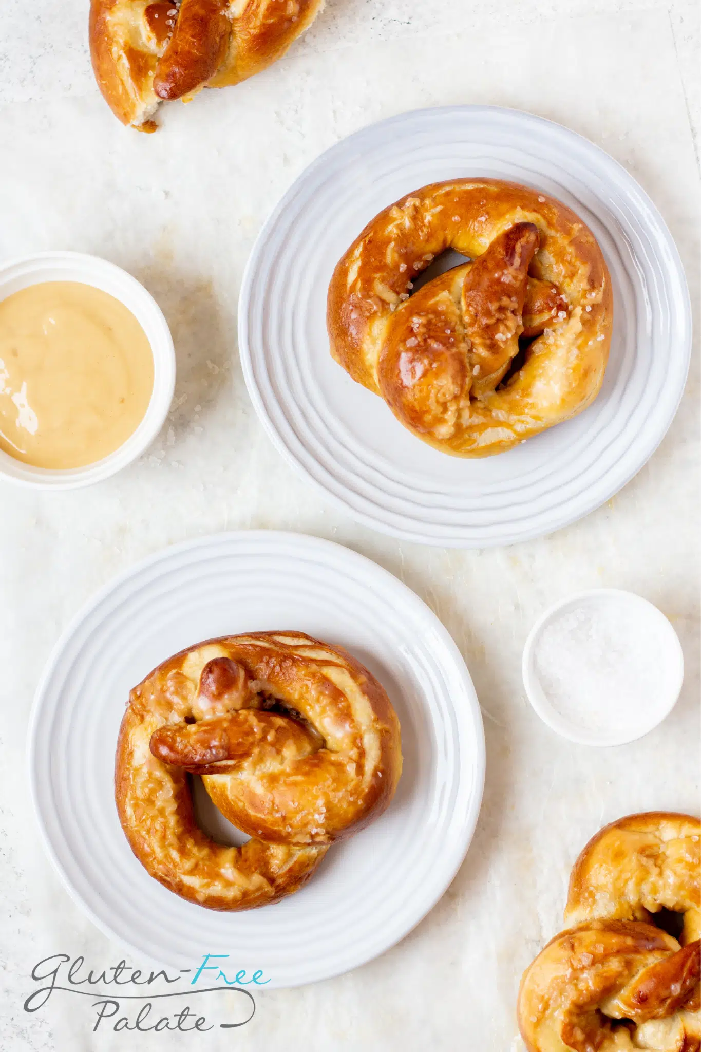 two gluten-free pretzels, each on a small white plate, viewed from above