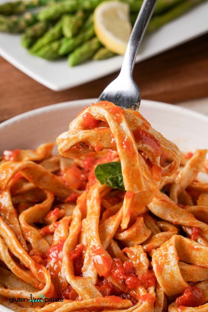 Gluten-free pasta in a bowl with pasta sauce and a fork taking some out.