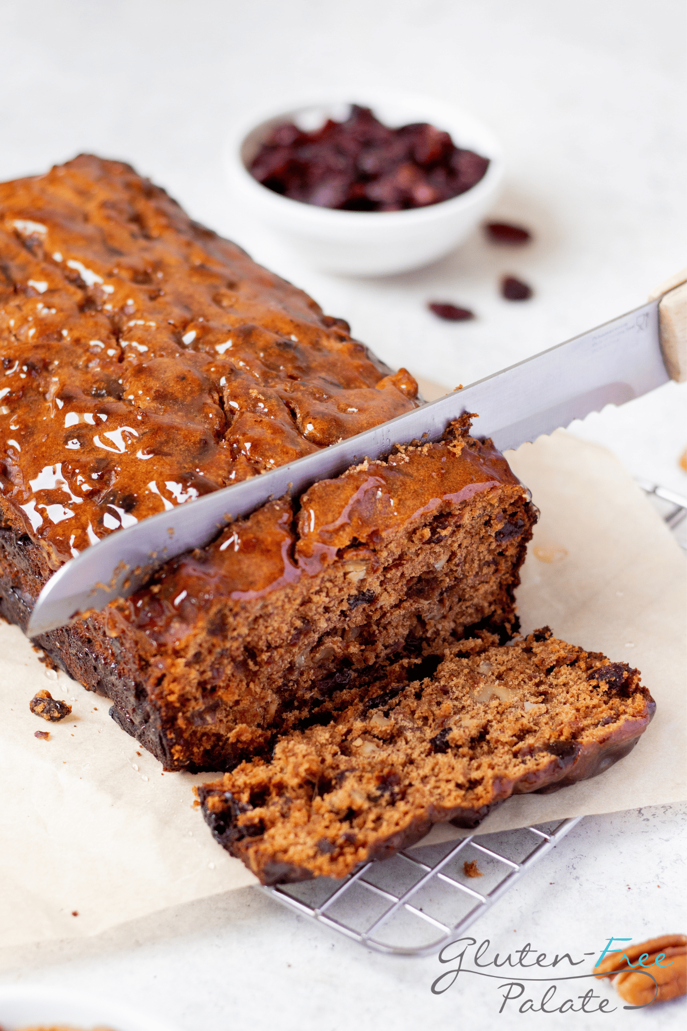 a loaf of gluten free fruit cake being sliced with a large serrated knife. 