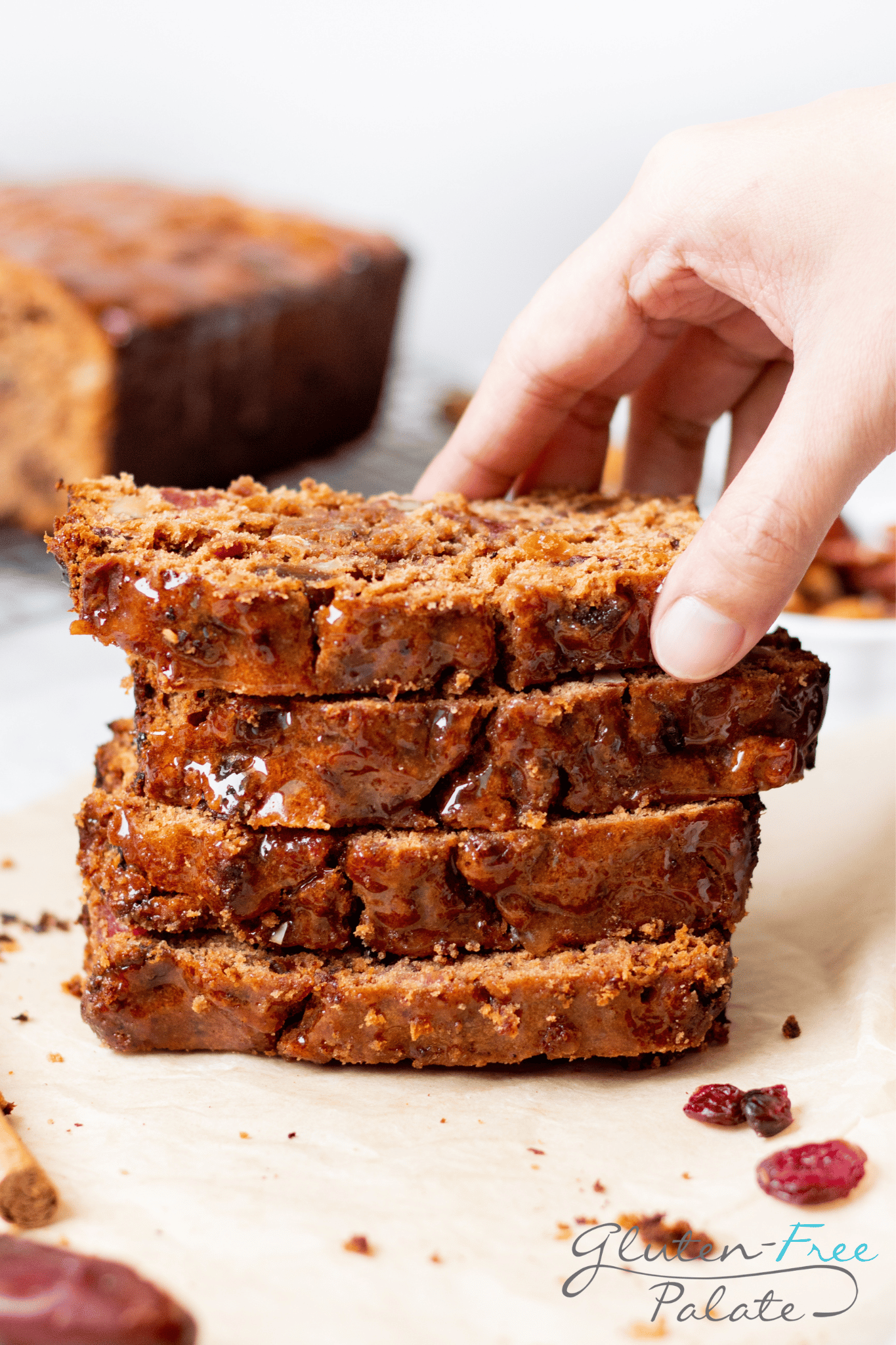 a stack of four slices of gluten free fruit cake. A hand is picking up the top slice.