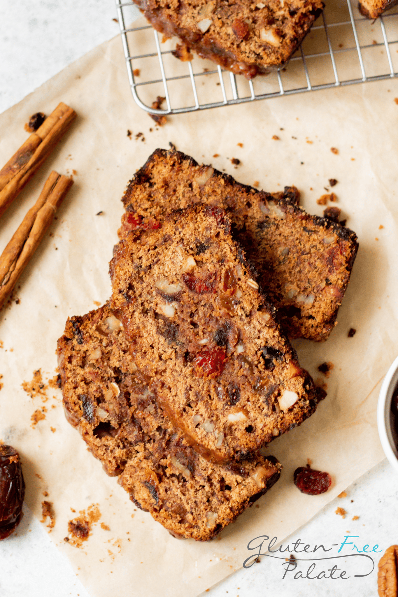 slices of fruit cake arranged on a cutting board, cinnamon sticks and dried cranberries are strewn around. 
