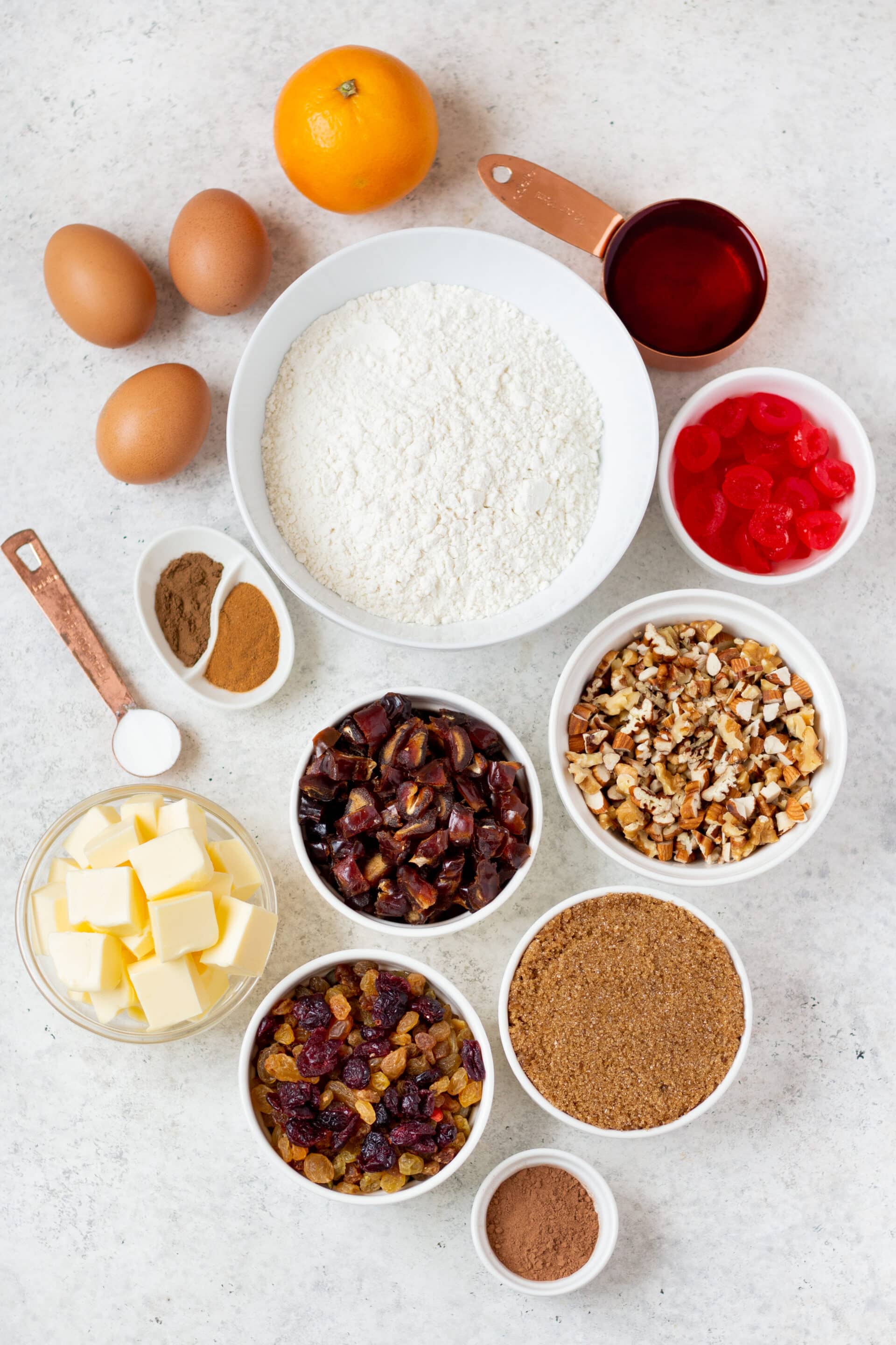 All of the ingredients for gluten free fruitcake, in separate bowls, on a counter, viewed from overhead