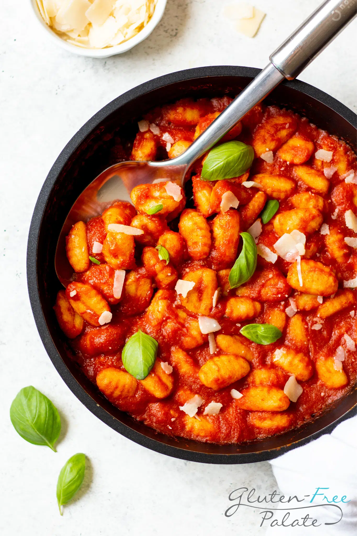 Gluten-free gnocchi in a pan of tomato sauce, garnished with basil and shaved cheese