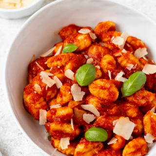 a bowl of gluten free gnocchi in tomato sauce garnished with parmesan cheese and fresh basil leaves