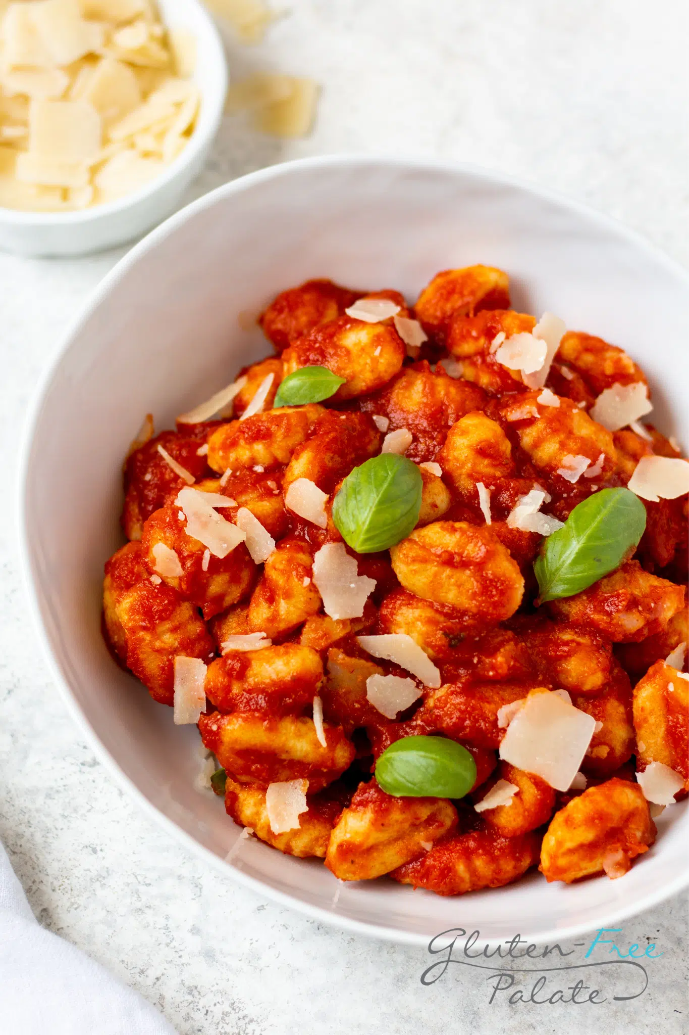 a bowl of gluten-free gnocchi in tomato sauce garnished with parmesan cheese and fresh basil leaves