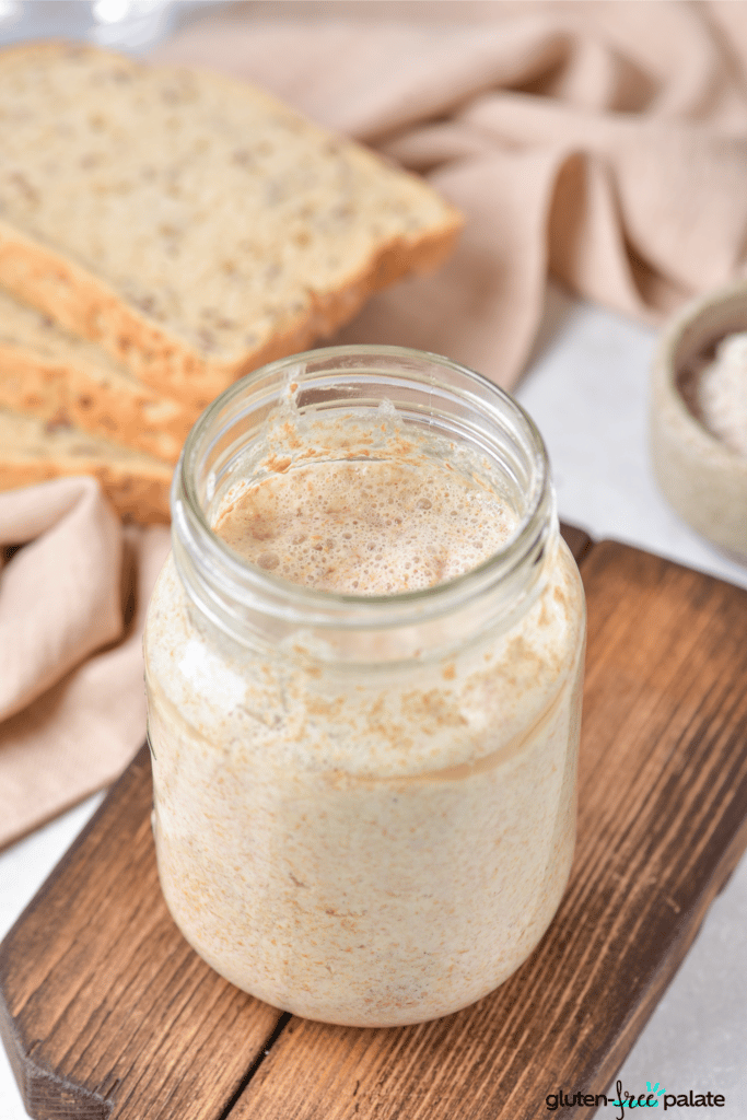 A jar of gluten-free sourdough starter with slices of bread in the background.