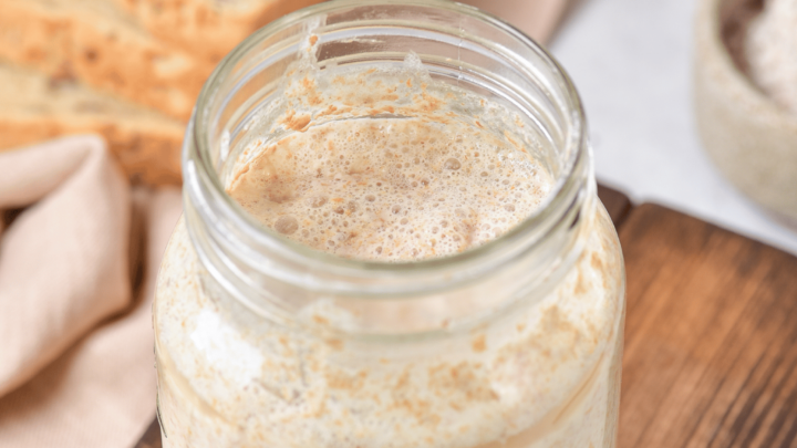 gluten-free sourdough starter in a jar with bread in the background.