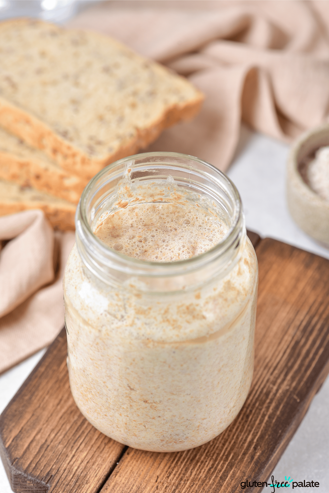 gluten-free sourdough starter in a jar with bread in the background.