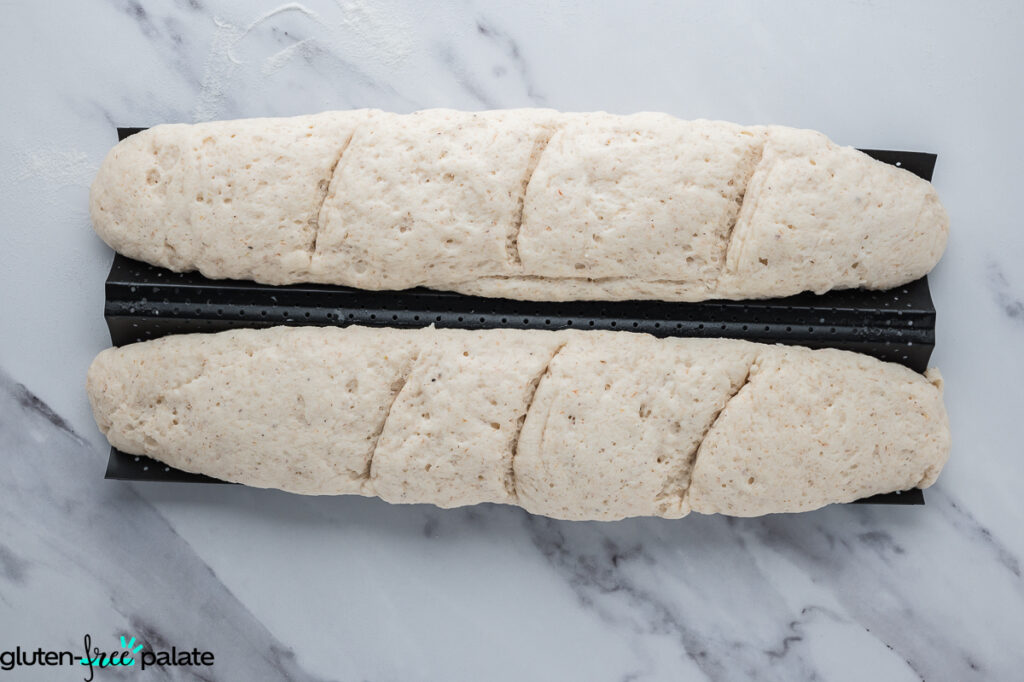Proofed baguette loaves on a perforated baguette pan, with 3 slices and ready to proof before baking.
