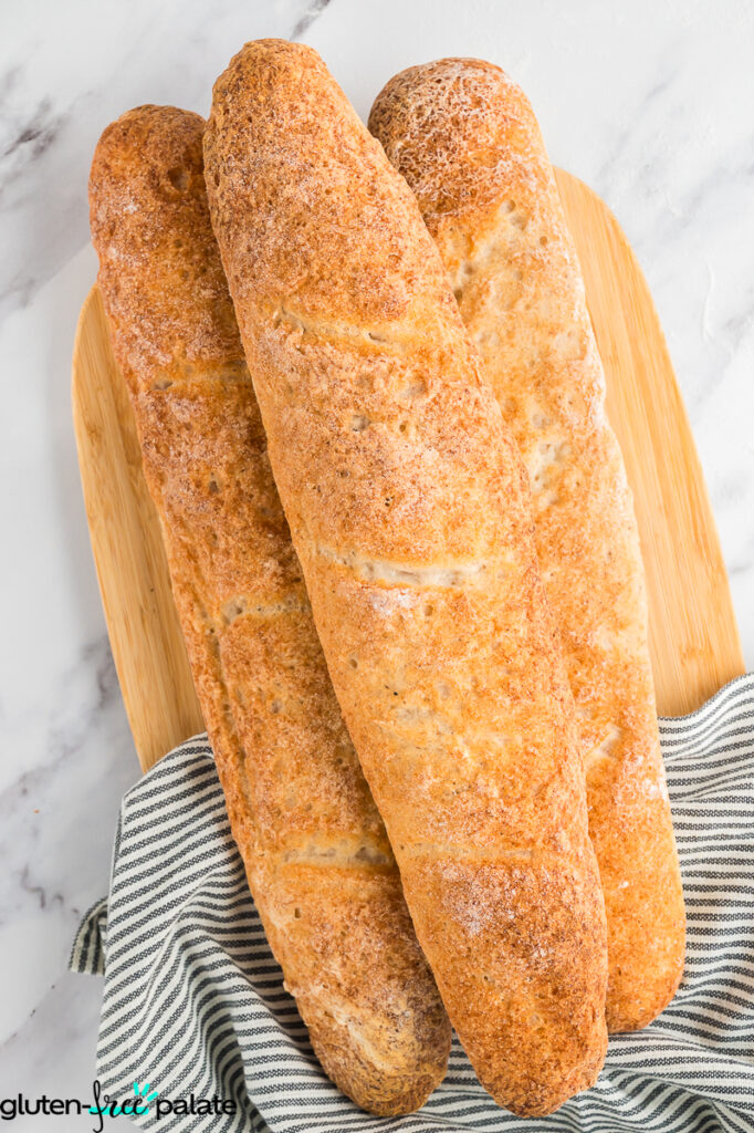 Loaves of baguette on a chopping board with a striped kitchen towel.